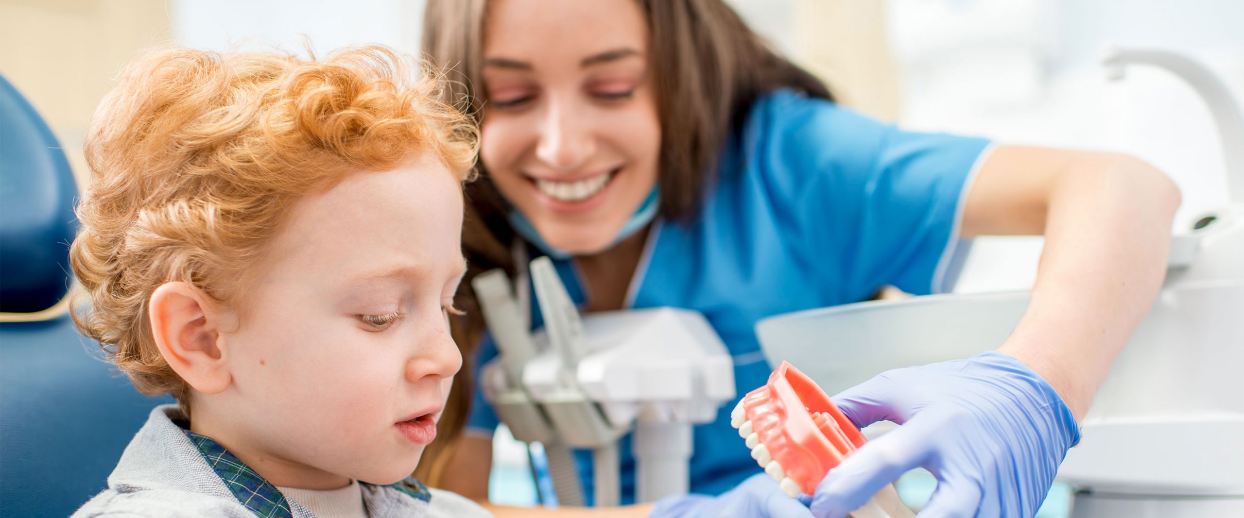 A red haired child looks at a mold of teeth with his dental hygenist
