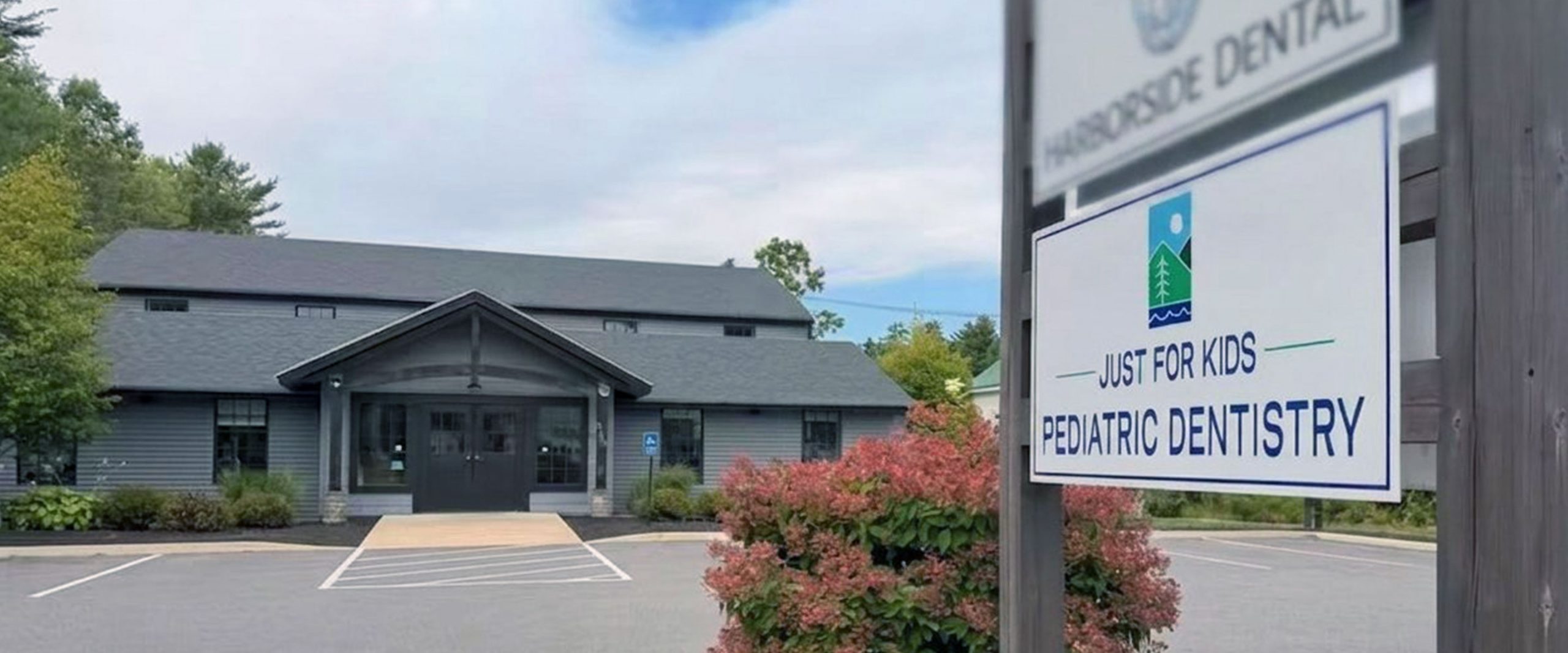 A brown building with plants and a sign in front displaying Just For Kids Pediatric Dentistry office in Wells Maine